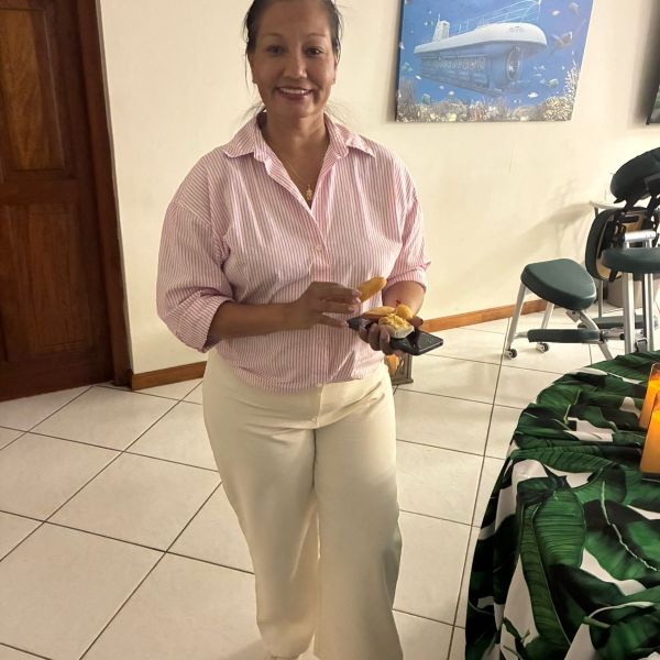 Woman in white pants and pink shirt holding food, standing indoors near a painting of a submarine.