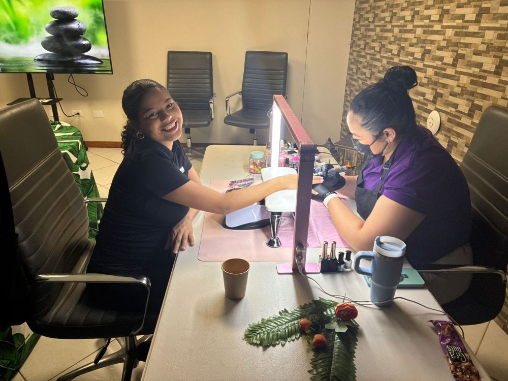 Two women at a nail salon, one smiling, getting a manicure from the other.