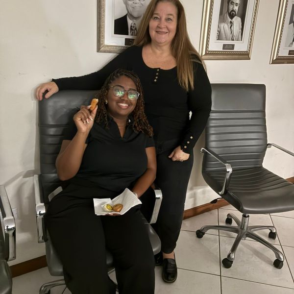 Two women in black outfits smiling near framed photos on the wall.