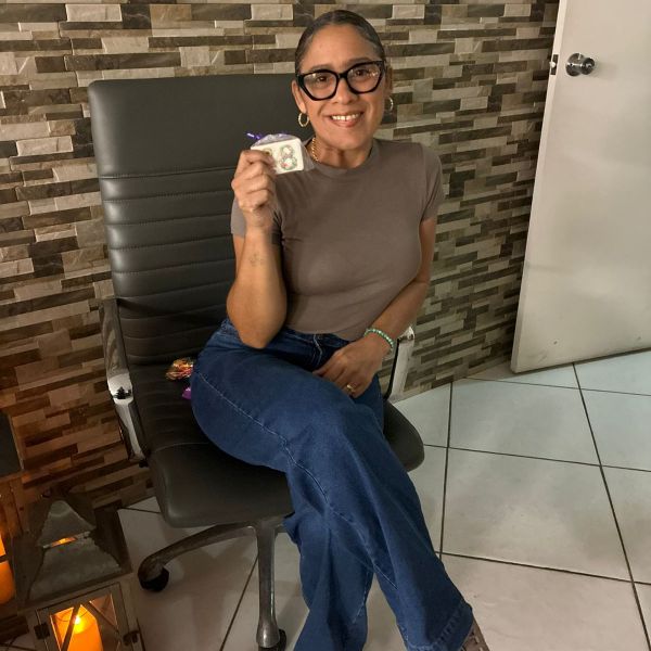 Person sitting in a chair, holding a small item, against a stone-patterned wall.