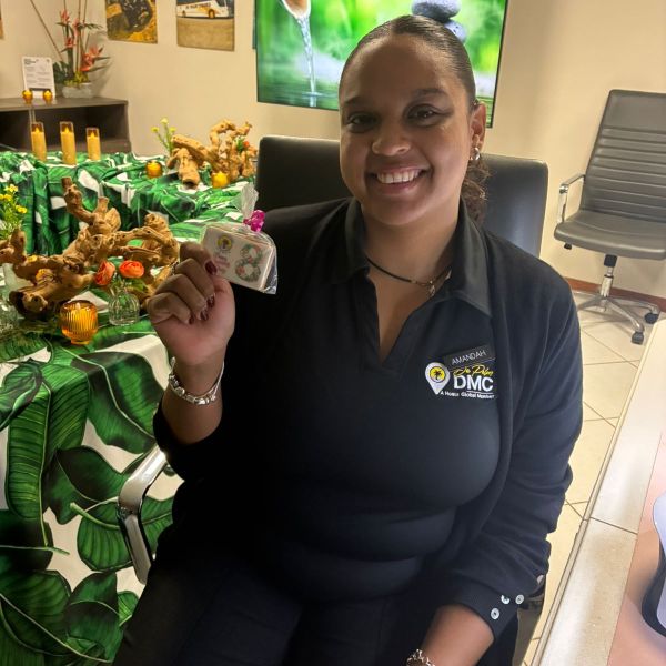Smiling person seated indoors, holding a small gift, with decorated table and nature photos in the background.