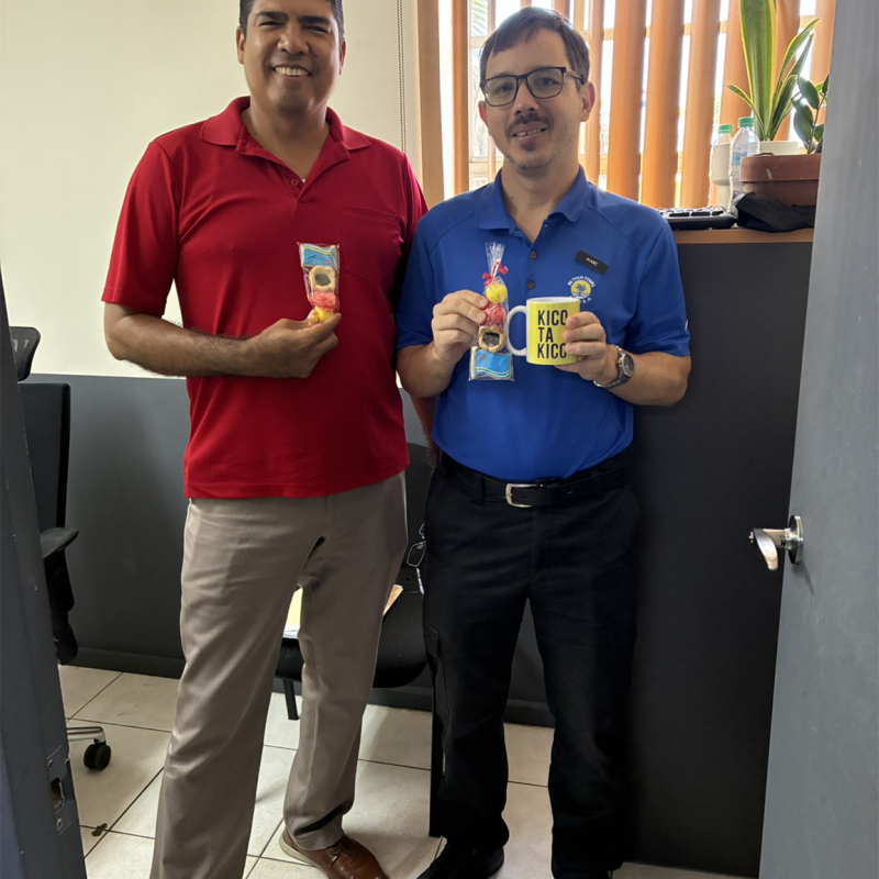 Two men in an office holding snacks, one in red shirt, one in blue.