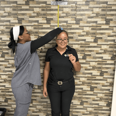 Person measuring another person's height against a tiled wall with a tape measure.