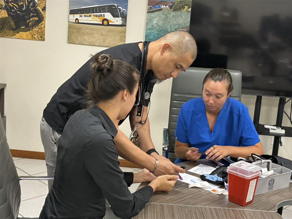 Three people in a room discussing medical items on a table.