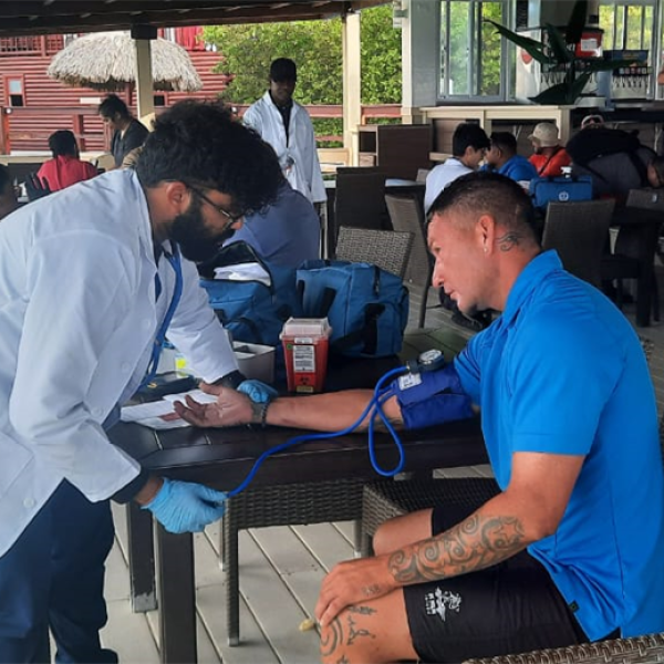 A doctor checks a man's blood pressure at an outdoor café by the sea.