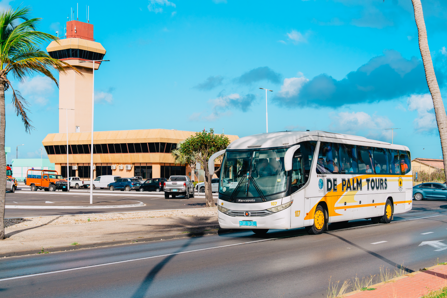 Tour bus passes control tower on sunny day with clear sky.