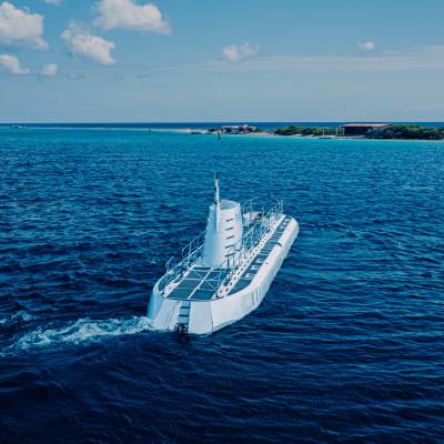 White submarine sailing on calm blue ocean under a clear sky.