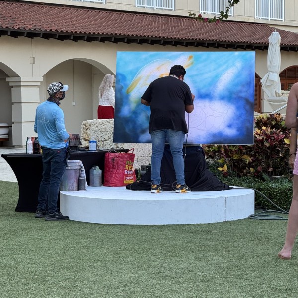 Artists painting on a large canvas outdoors on a round platform.