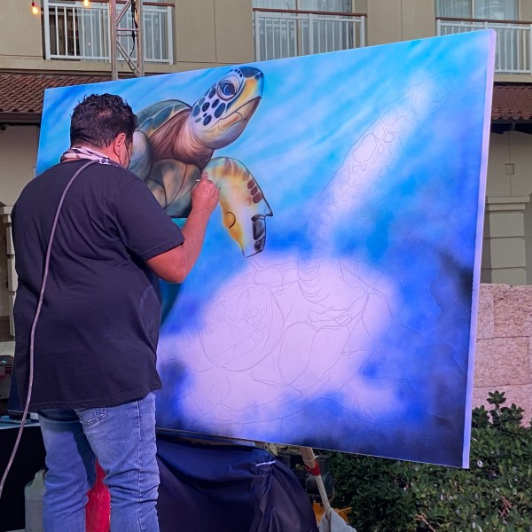 Artist painting a large sea turtle mural outdoors.