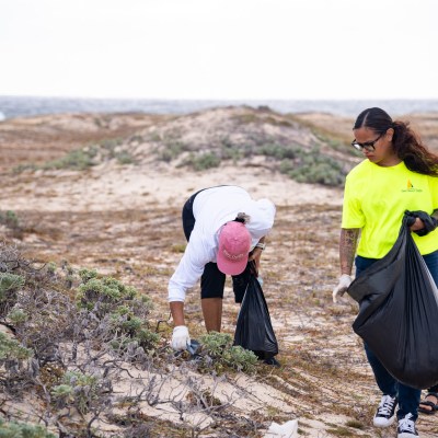 Three people picking up trash on a beach with large garbage bags.