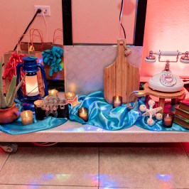 Decorative setup with vintage phone, camera, lantern, and books on blue fabric with candles.