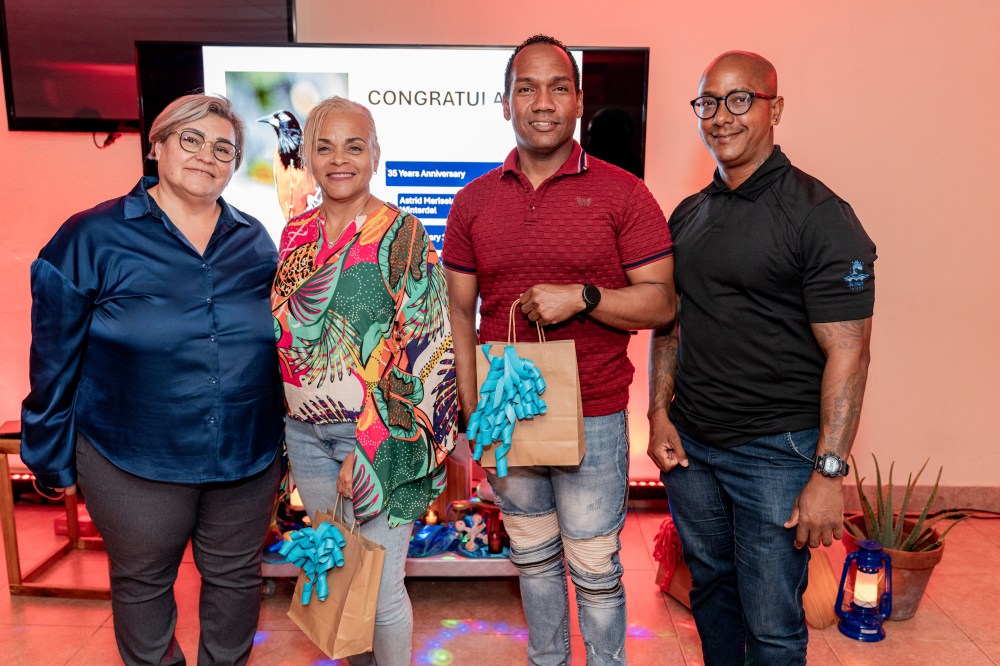 Four people posing at an indoor event, two holding gift bags with blue ribbons.