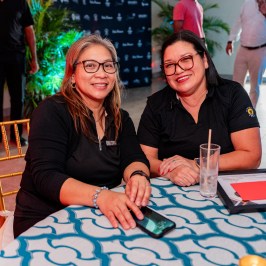 Two women smiling at a table with a blue patterned tablecloth.