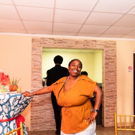 Smiling person in orange shirt poses near a decorated table indoors.