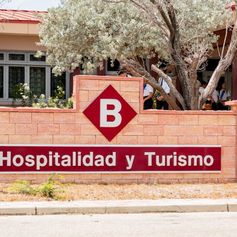 Sign for Hospitalidad y Turismo with a 'B' on a brick wall.