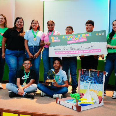 Group of students and adults with a check and project display, celebrating a competition win.