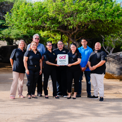 Group of people outdoors holding a sign, with trees and rocks in the background.