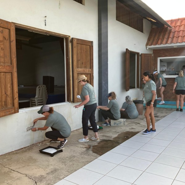 Volunteers painting a building exterior with open windows.