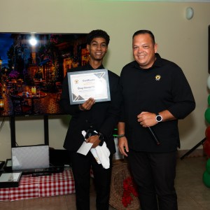 Two men stand smiling, one holding a certificate indoors.