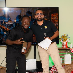 Two men smiling and posing with awards in front of a large screen indoors.