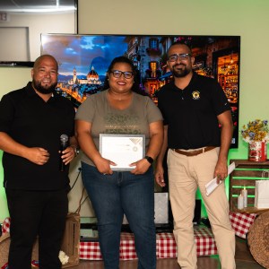 Three people standing, one holding a certificate, with a decorated background.