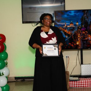 Person holding a certificate, standing near a balloon decoration and a large display showing a cityscape.