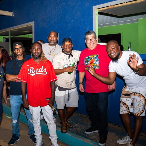 Group of men smiling and posing in front of a blue wall outdoors at night.