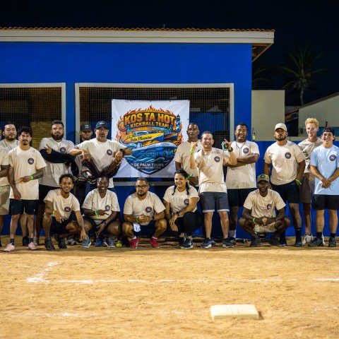 Group of people in matching shirts posing on a baseball field at night.