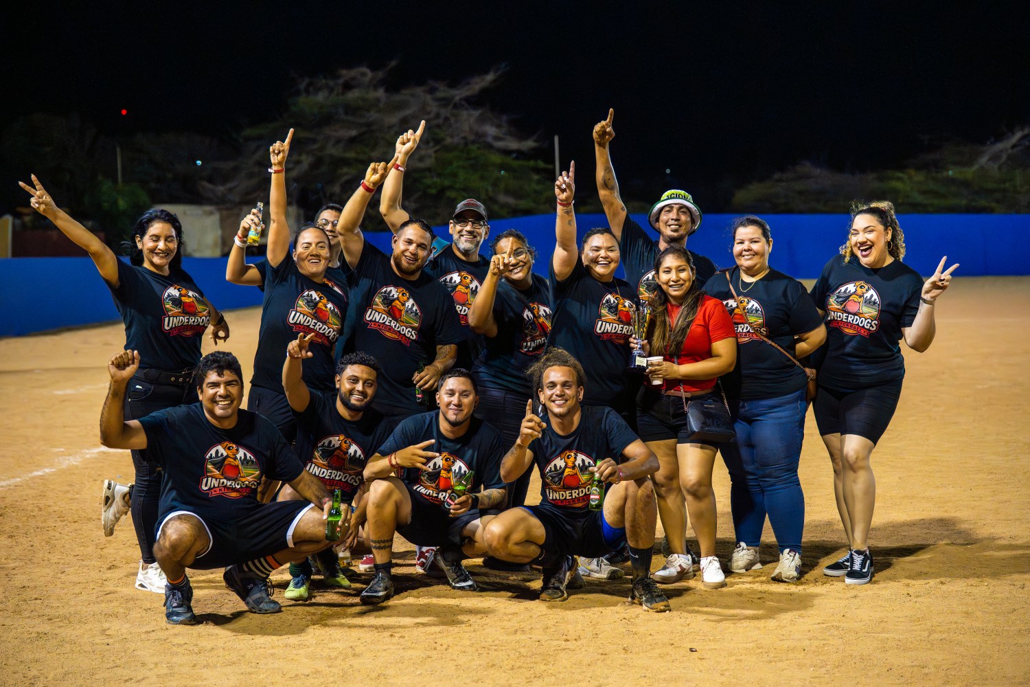 Group of people in matching shirts celebrating on a sports field at night.