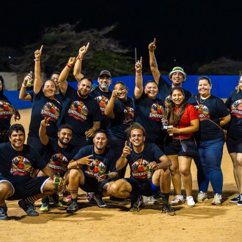 Group of people in matching shirts celebrating on a baseball field at night.