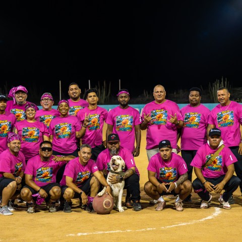 Group of people in pink shirts posing on a baseball field, one holding a dog.