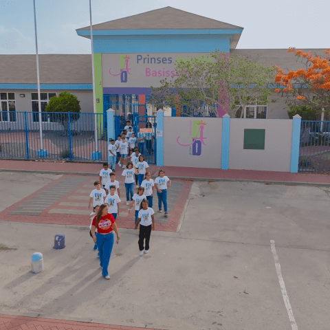 Group of students in uniform exiting a school building with trees and a bright sky.