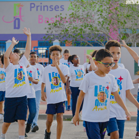 Children wearing white shirts gather and play outside a school building.