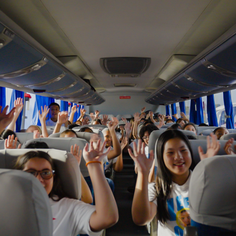 Bus interior with people raising hands, blue curtains.