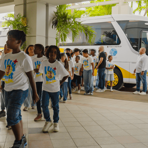 Children in white shirts form a line to board a white bus.