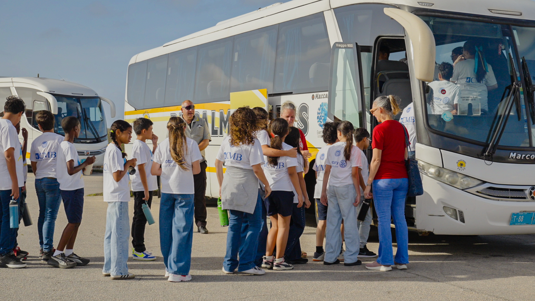 Children and adults boarding a white bus on a sunny day.