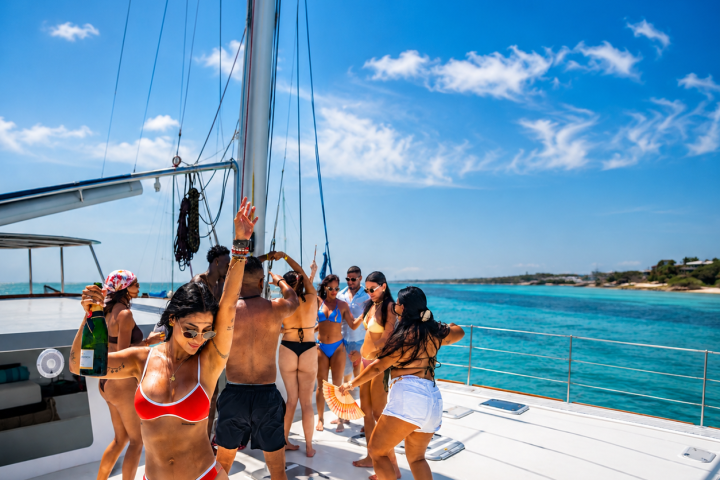 Group of people dancing on a boat in swimsuits under a clear blue sky.