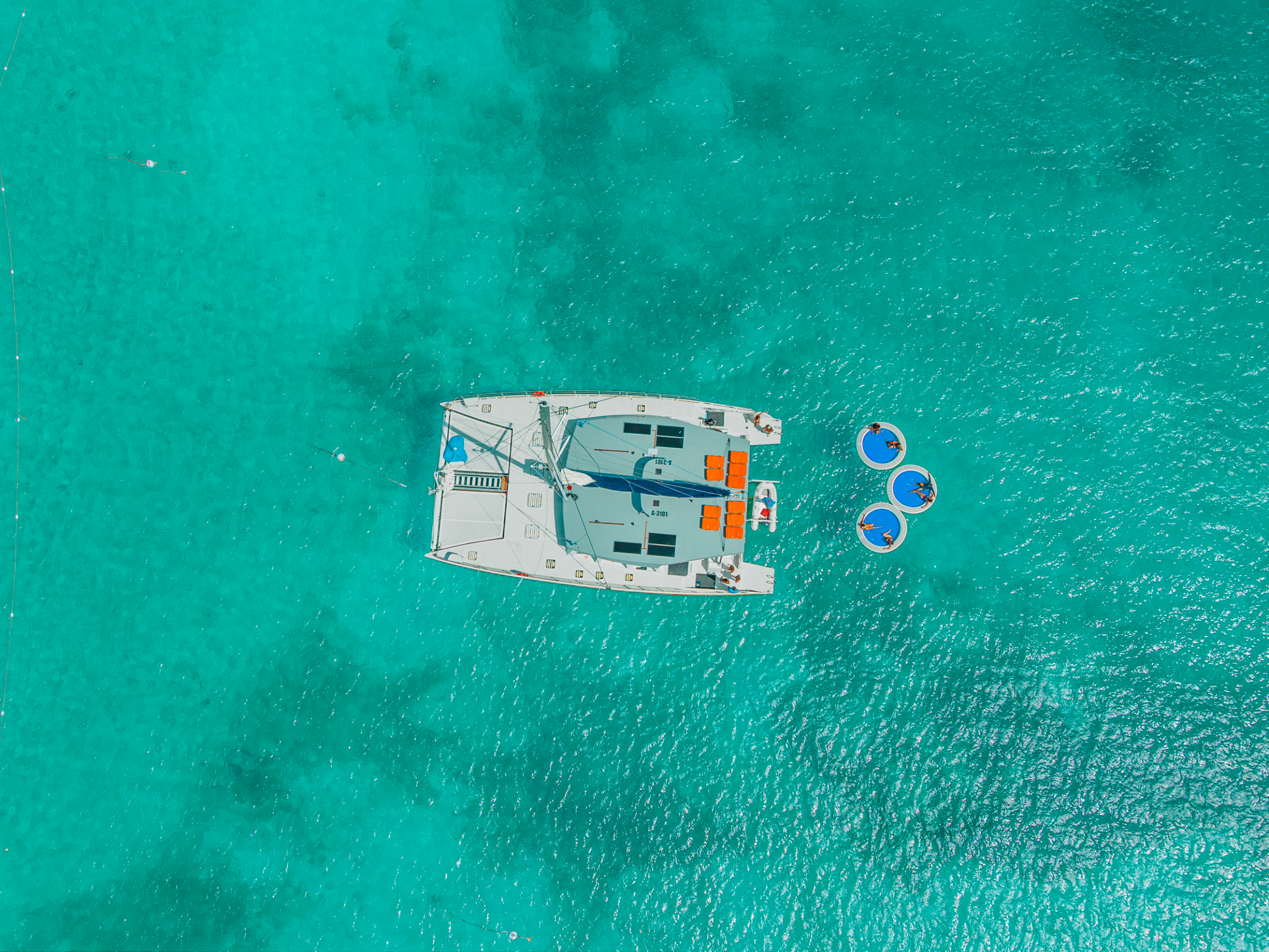 Aerial view of a catamaran and floats on clear turquoise water.