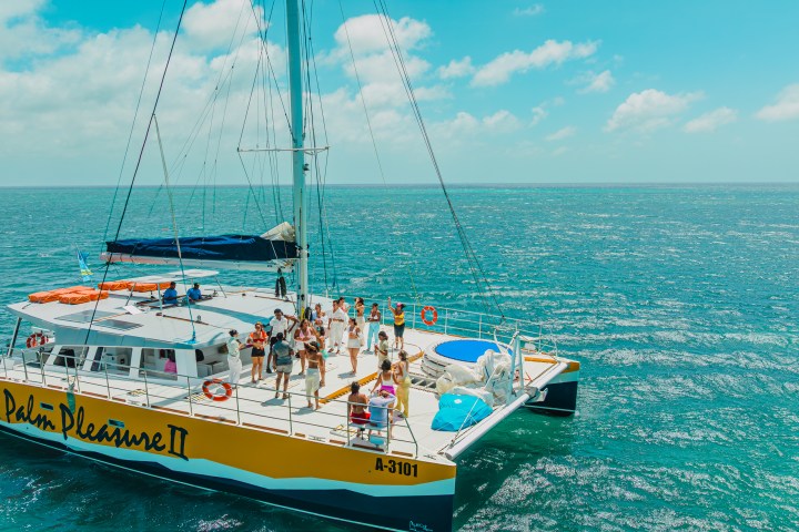 People on a large catamaran boat in calm blue sea under clear skies.