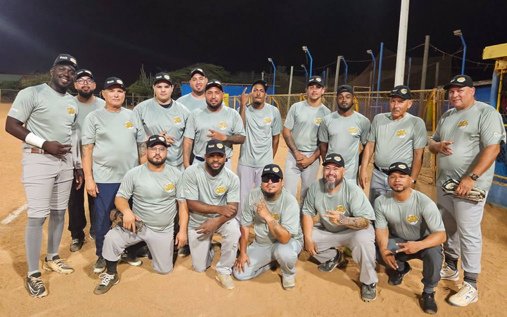 Baseball team poses on field at night, all wearing matching light blue shirts.