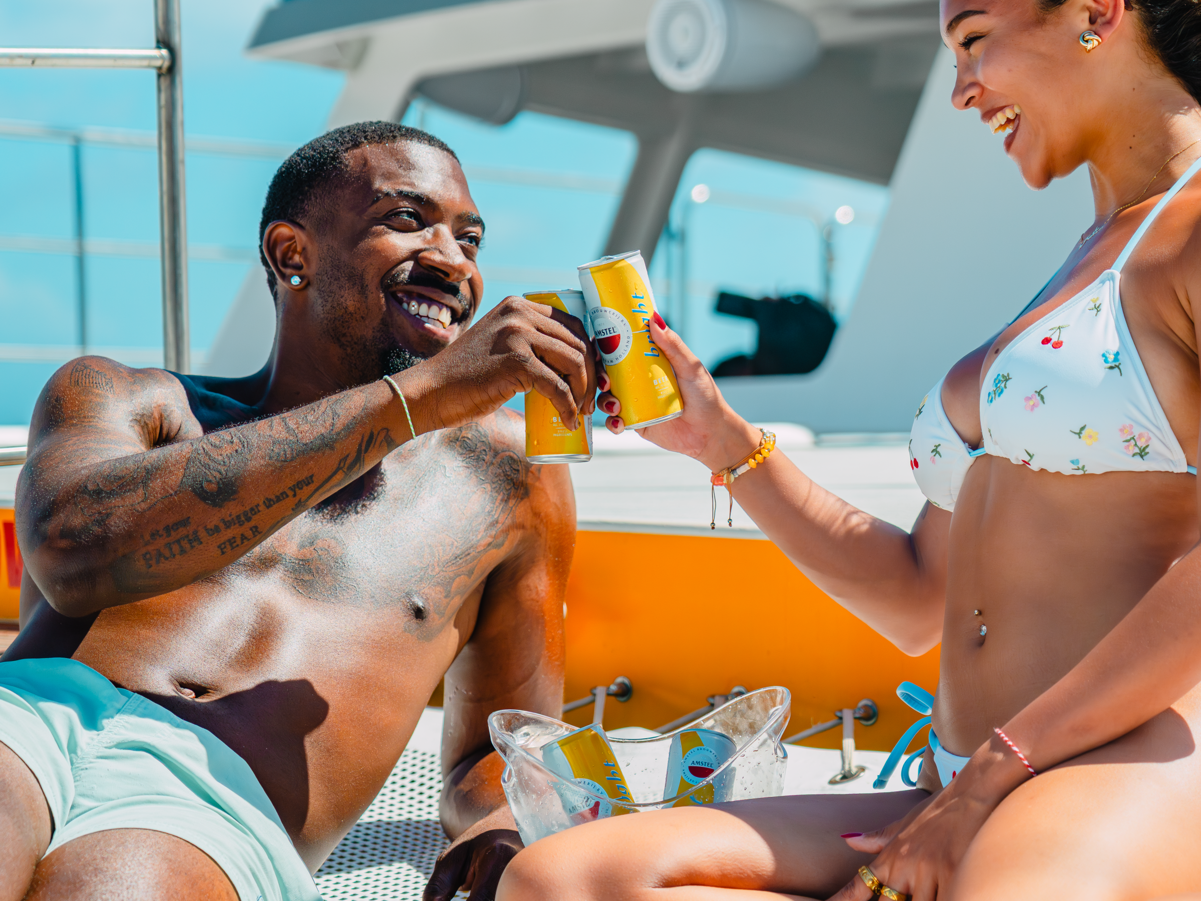 Two people toasting drinks on a boat, wearing swimwear.