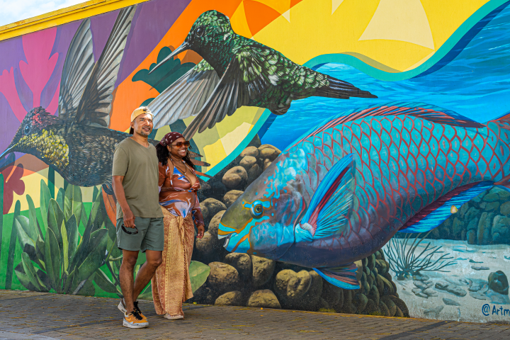 Couple posing by colorful mural with birds, fish, and plants.