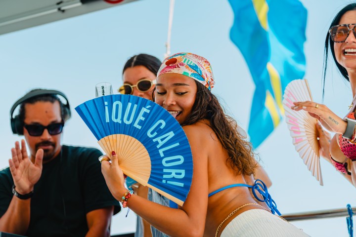 People enjoying a boat party, holding fans, with flags in the background.