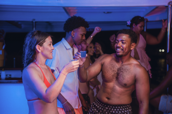 Group of people on a boat at night, holding drinks and socializing.