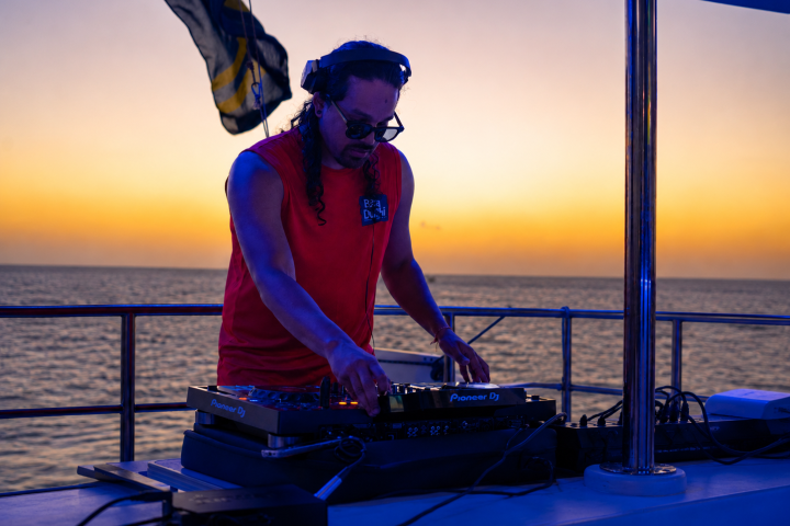 DJ playing music on a boat at sunset.