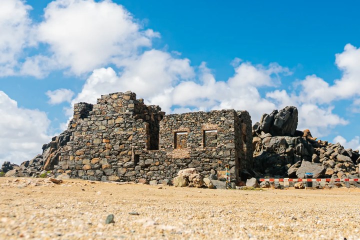 Ruined stone building on rocky terrain under blue sky.
