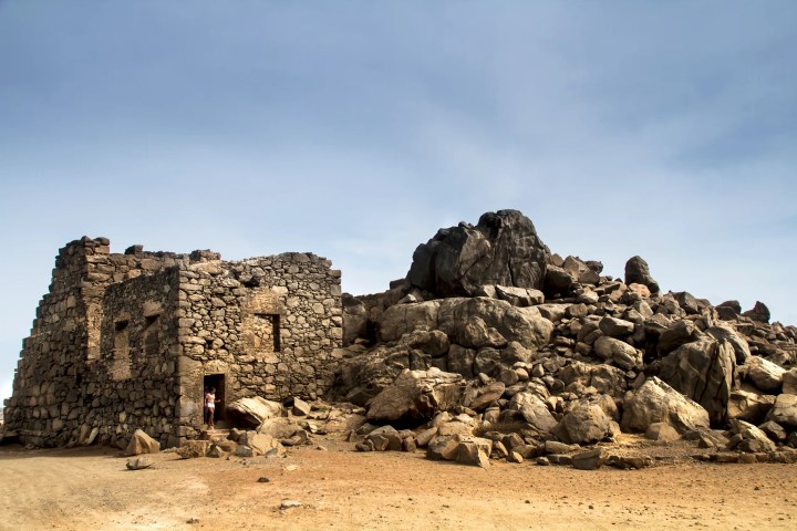 Old stone building and rocky mound under clear blue sky.