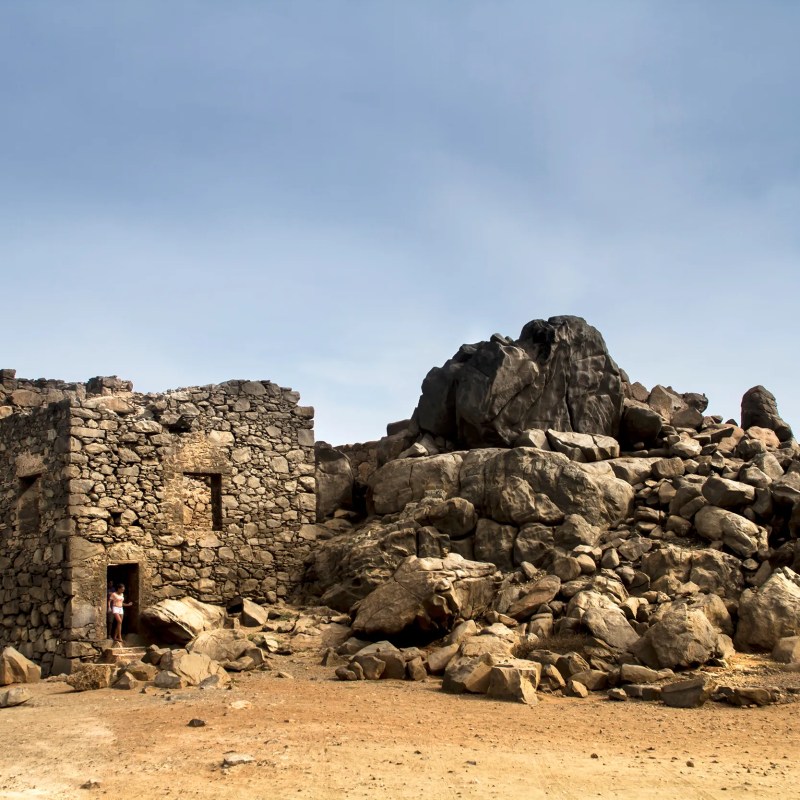 Old stone building and rocky mound under clear blue sky.