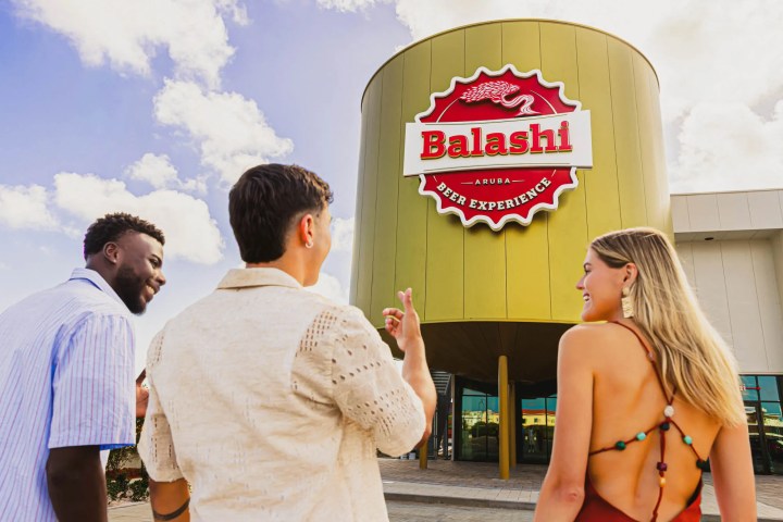 Three people outside a building with a large 'Balashi Beer Experience' sign.