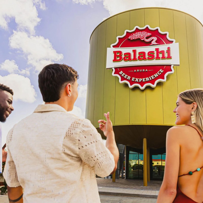 Three people outside a building with a large 'Balashi Beer Experience' sign.